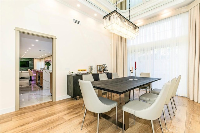 dining room featuring light wood-type flooring, a chandelier, and a towering ceiling