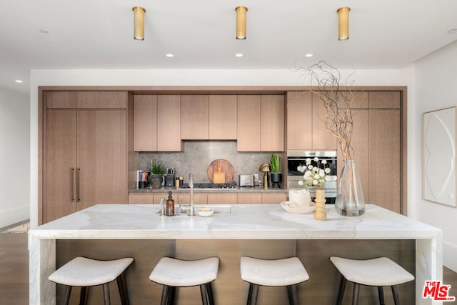 kitchen with tasteful backsplash, black gas stovetop, a center island with sink, wood-type flooring, and light stone countertops