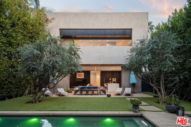 back house at dusk featuring a patio area and a yard