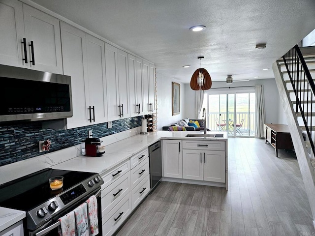 kitchen featuring pendant lighting, kitchen peninsula, sink, white cabinetry, and stainless steel appliances