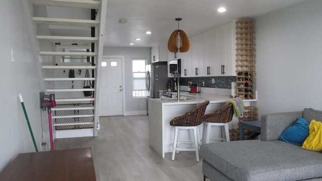 kitchen with white cabinetry, kitchen peninsula, stainless steel appliances, light wood-type flooring, and hanging light fixtures