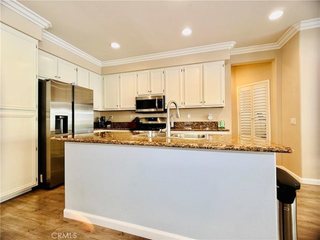 kitchen with sink, appliances with stainless steel finishes, dark stone countertops, white cabinets, and a center island with sink