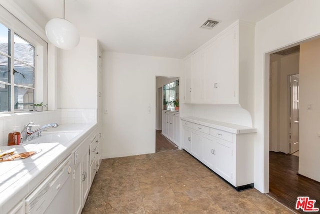 kitchen with sink, white cabinetry, hanging light fixtures, tile counters, and white dishwasher