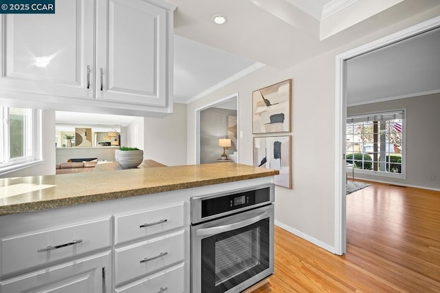 kitchen with stainless steel oven, white cabinets, light wood-type flooring, and crown molding