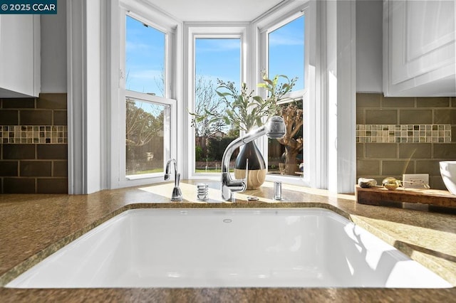 interior details featuring stone counters, white cabinetry, tasteful backsplash, and sink