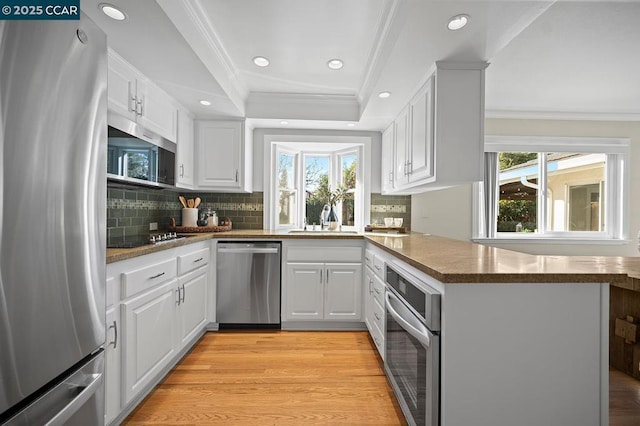 kitchen with kitchen peninsula, appliances with stainless steel finishes, white cabinetry, and ornamental molding