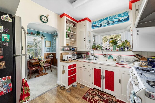 kitchen with white cabinets, light wood-type flooring, gas range gas stove, sink, and stainless steel fridge