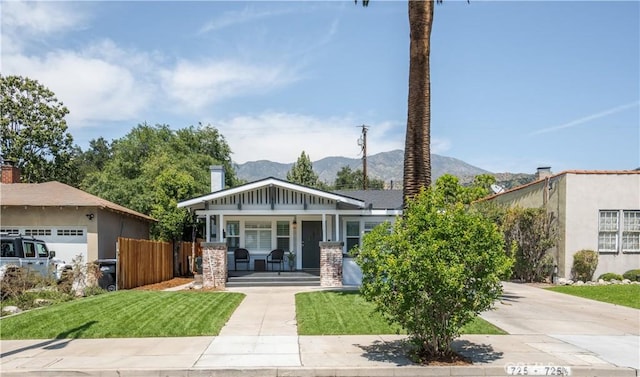 view of front facade with covered porch, a garage, a front lawn, and a mountain view