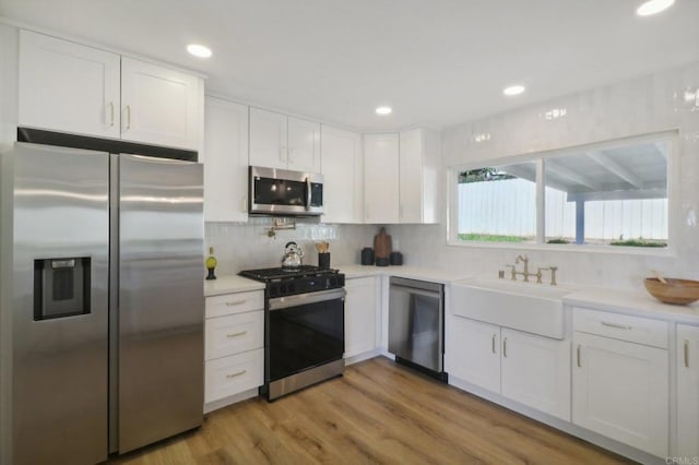 kitchen featuring stainless steel appliances, backsplash, white cabinets, light hardwood / wood-style flooring, and sink