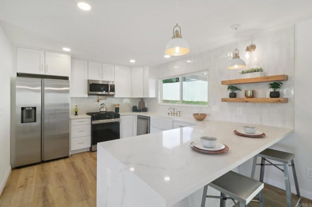 kitchen with pendant lighting, white cabinets, appliances with stainless steel finishes, a kitchen bar, and kitchen peninsula