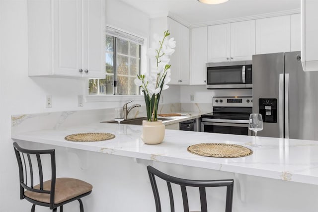 kitchen featuring stainless steel appliances, white cabinetry, a breakfast bar area, and light stone counters