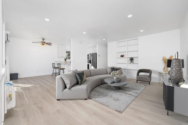 living room featuring built in shelves, light hardwood / wood-style floors, and ceiling fan