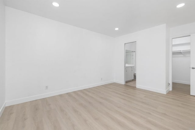 unfurnished bedroom featuring ensuite bathroom, a spacious closet, a closet, and light wood-type flooring