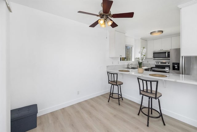 kitchen with appliances with stainless steel finishes, white cabinets, a kitchen breakfast bar, kitchen peninsula, and light hardwood / wood-style flooring