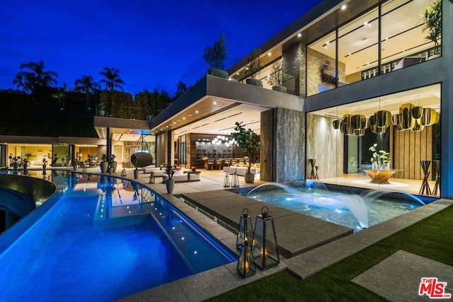 pool at night with a jacuzzi and pool water feature