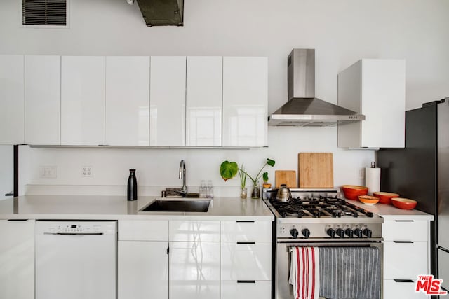 kitchen featuring sink, appliances with stainless steel finishes, wall chimney range hood, and white cabinetry