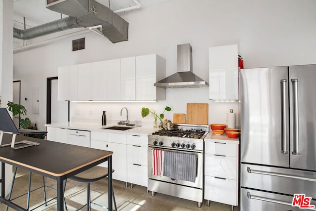 kitchen featuring sink, wall chimney range hood, appliances with stainless steel finishes, and white cabinets