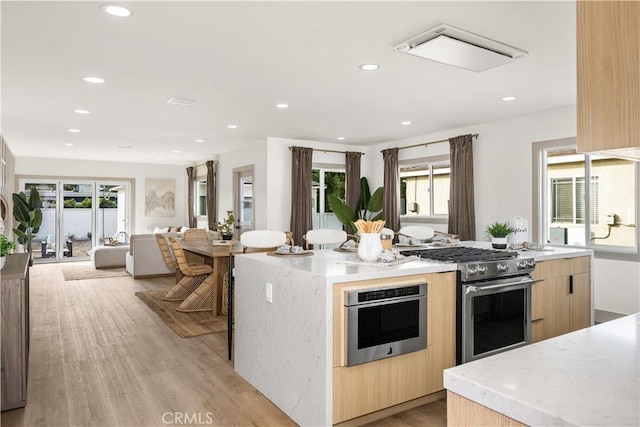 kitchen with a kitchen island, appliances with stainless steel finishes, light brown cabinets, and light hardwood / wood-style floors