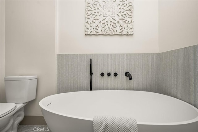 full bathroom featuring a wainscoted wall, a freestanding tub, and toilet