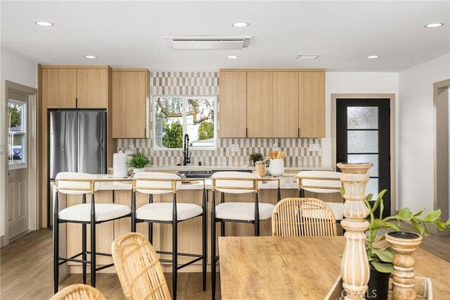 kitchen featuring tasteful backsplash, freestanding refrigerator, light countertops, and light brown cabinetry