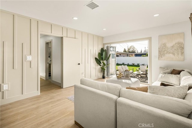 living room featuring light wood-type flooring, visible vents, a decorative wall, and recessed lighting