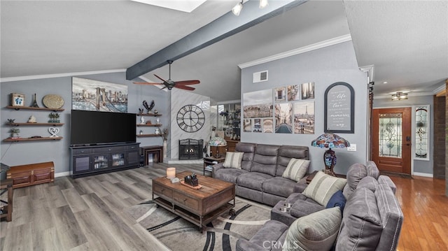 living room featuring ceiling fan, lofted ceiling with beams, wood-type flooring, crown molding, and a wood stove