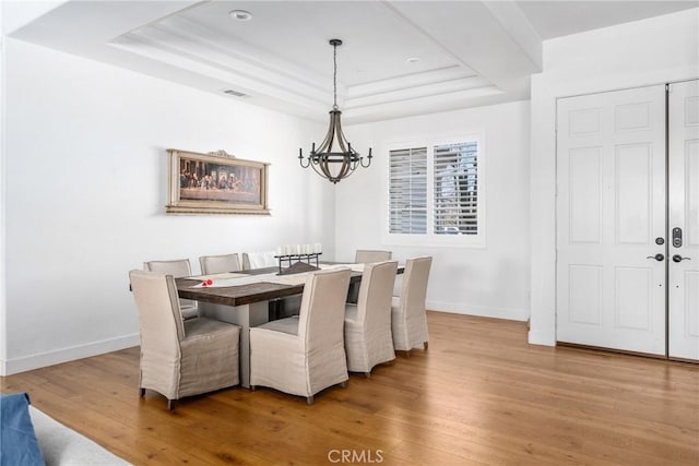 dining space featuring light hardwood / wood-style flooring, a raised ceiling, and a notable chandelier