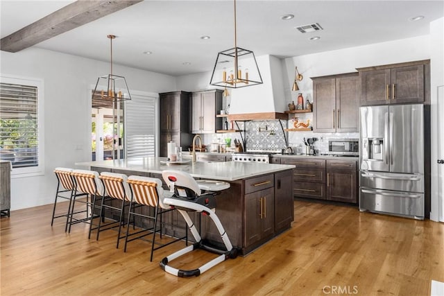 kitchen with tasteful backsplash, stainless steel appliances, beamed ceiling, and a kitchen island with sink