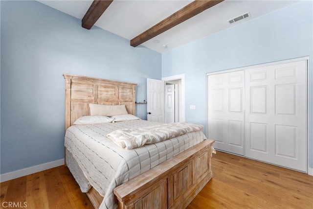 bedroom featuring light wood-type flooring, a closet, and beamed ceiling