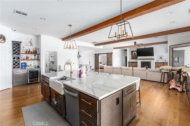 kitchen with stainless steel dishwasher, sink, beamed ceiling, hanging light fixtures, and a kitchen island with sink