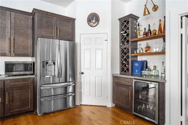 kitchen with dark brown cabinets, appliances with stainless steel finishes, beverage cooler, and hardwood / wood-style flooring