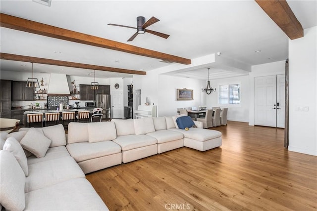 living room featuring ceiling fan with notable chandelier, wood-type flooring, and beam ceiling