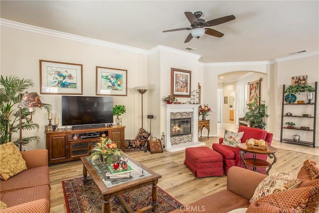 living room with ceiling fan, a stone fireplace, ornamental molding, and light hardwood / wood-style floors