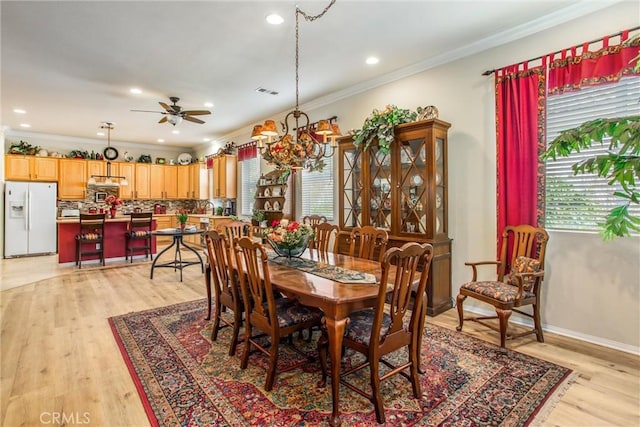 dining space featuring crown molding, light wood-type flooring, plenty of natural light, and ceiling fan with notable chandelier