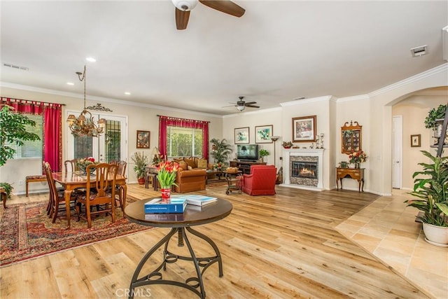 living room featuring light wood-type flooring, ornamental molding, and ceiling fan with notable chandelier