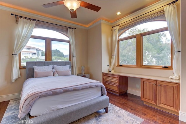 bedroom with ceiling fan, dark hardwood / wood-style flooring, built in desk, and ornamental molding