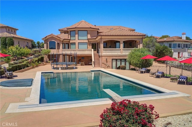 rear view of house featuring a fenced in pool, a balcony, and a patio