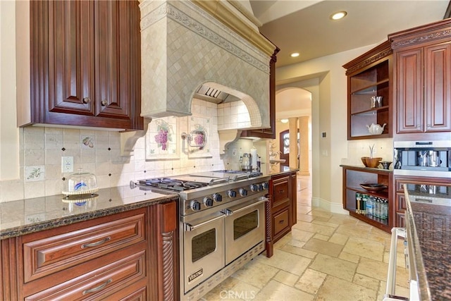 kitchen featuring double oven range, backsplash, and dark stone countertops