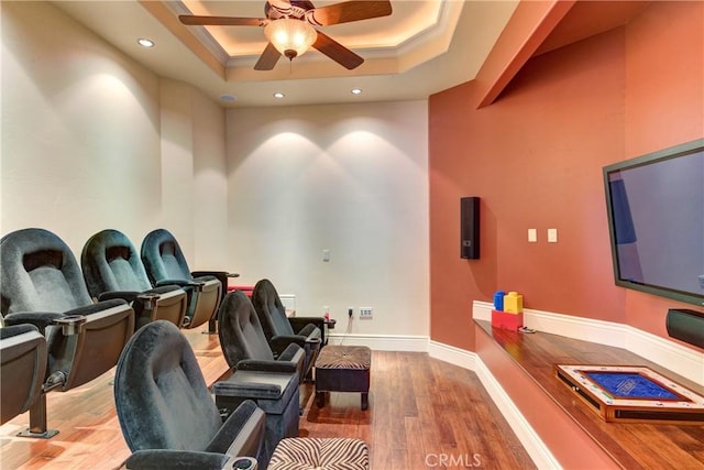 home theater room featuring ceiling fan, ornamental molding, wood-type flooring, and a raised ceiling