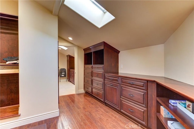 corridor with light hardwood / wood-style floors and lofted ceiling with skylight