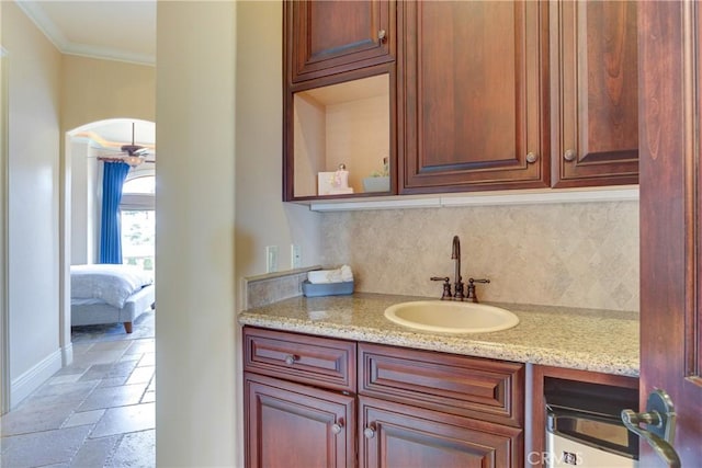 interior space featuring light stone counters, sink, decorative backsplash, and crown molding