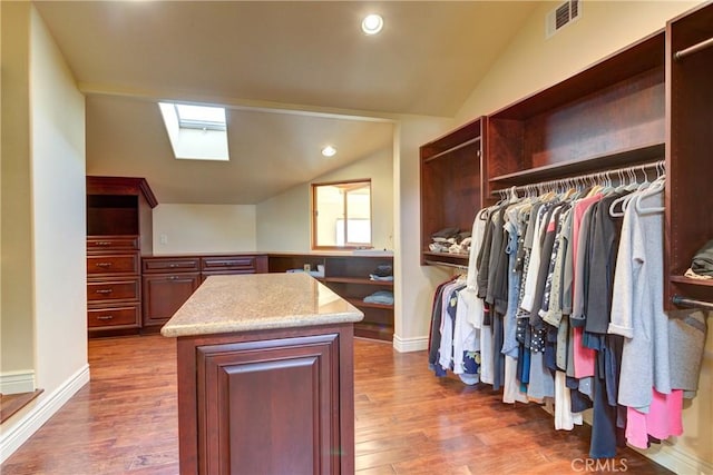 spacious closet with dark wood-type flooring and vaulted ceiling with skylight