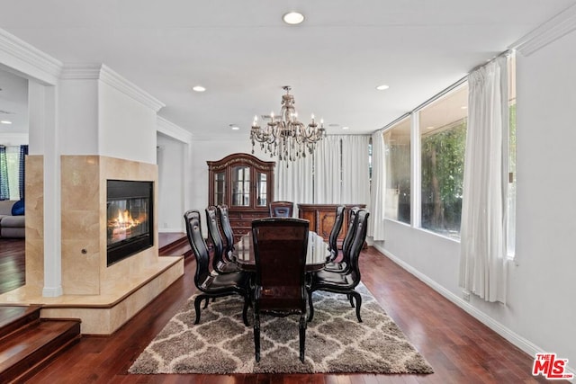 dining area featuring dark wood-type flooring, ornamental molding, a tiled fireplace, and an inviting chandelier