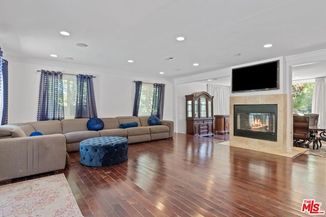 living room featuring a healthy amount of sunlight, dark wood-type flooring, a tile fireplace, and crown molding