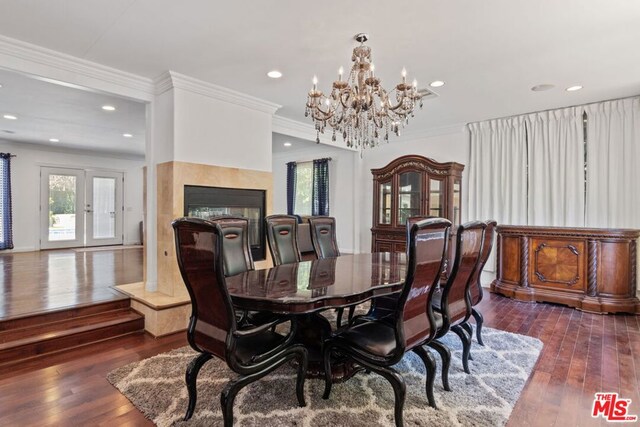 dining area featuring dark hardwood / wood-style floors, a tile fireplace, ornamental molding, and a notable chandelier