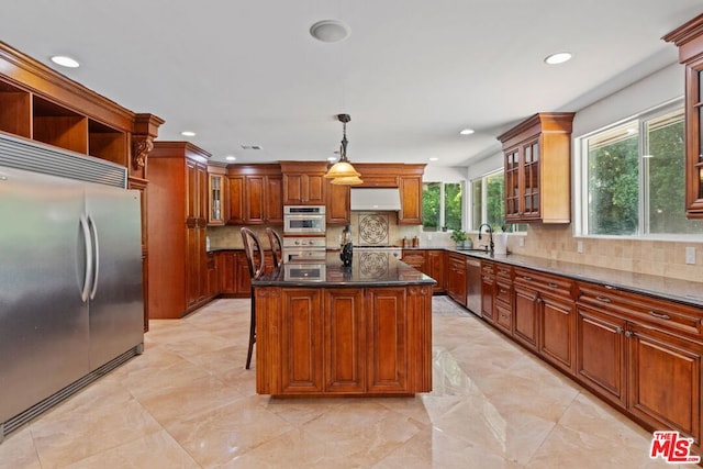 kitchen with appliances with stainless steel finishes, a center island, decorative light fixtures, dark stone countertops, and backsplash