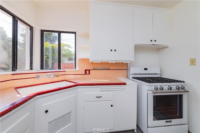 kitchen with sink, white cabinetry, white gas stove, and tile counters