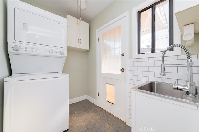 clothes washing area with stacked washer and dryer, cabinets, light tile patterned floors, and sink