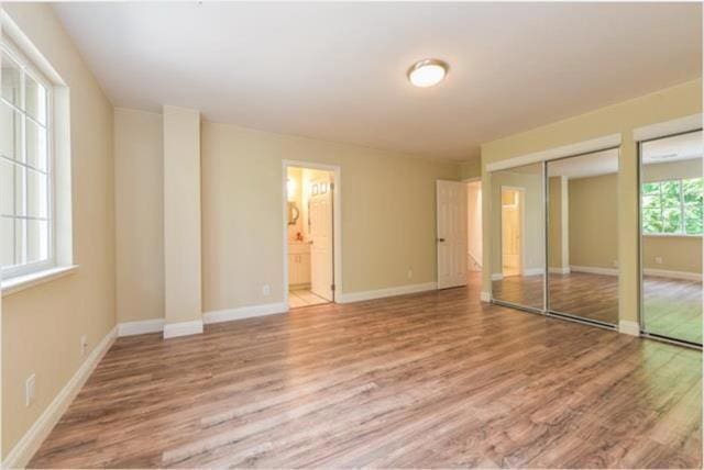 unfurnished bedroom featuring ensuite bathroom, two closets, and hardwood / wood-style flooring