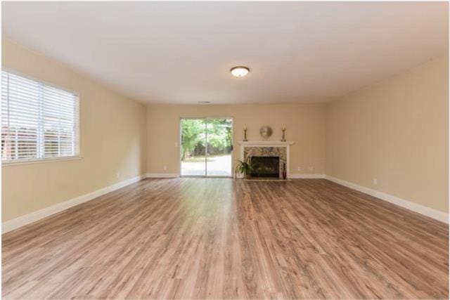 unfurnished living room with light wood-type flooring, a high end fireplace, and a healthy amount of sunlight